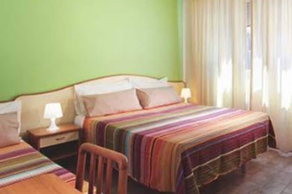 Una habitación de hotel con cama, una silla, una mesita de noche y una lámpara.