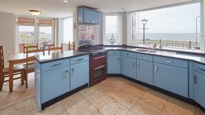 A kitchen with blue cabinets, a stove, and a large window overlooking the sea. - Host & Stay | Sunset View (Whitby)