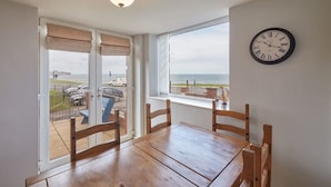 A dining area with a wooden table and chairs, a clock on the wall, and a view of the sea through large windows. - Host & Stay | Sunset View (Whitby)