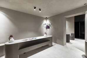 A modern reception area with a minimalist design, featuring a reception desk, a vase with flowers, and a magazine. - Elysium Suites Collection (Rome)