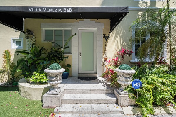 A hotel entrance with a black awning, a white door, and steps leading up to it. - Villa Venezia BB (Miami Beach)