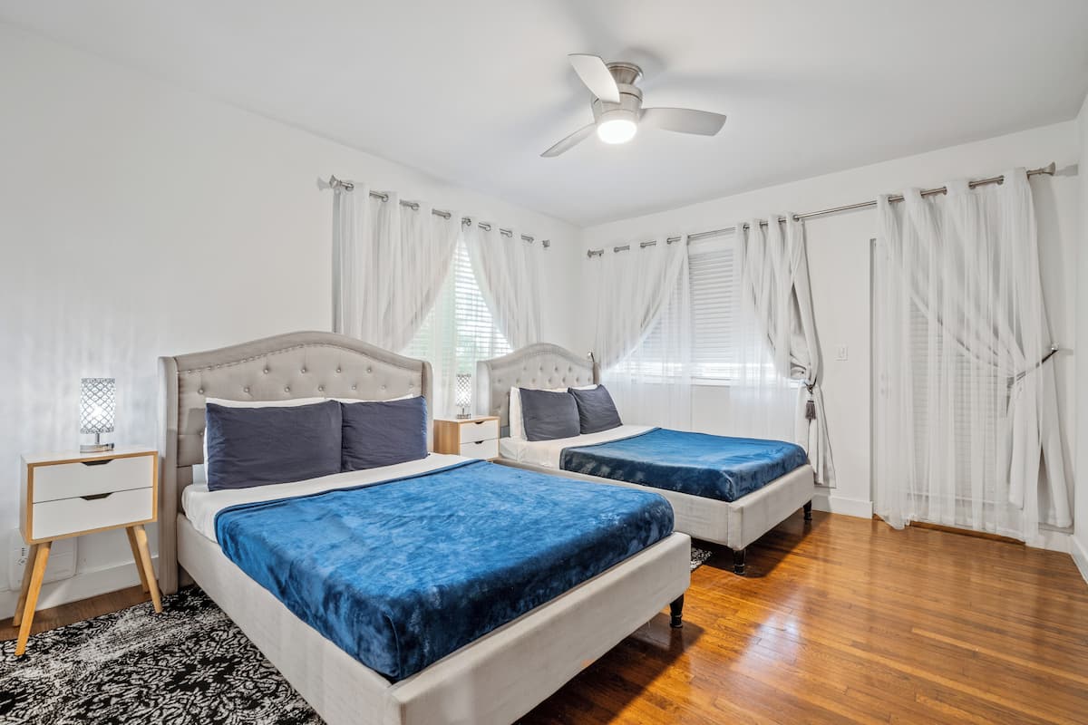 A bedroom with two beds, a ceiling fan, and white curtains.