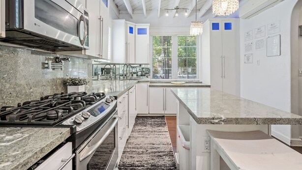A modern kitchen with stainless steel appliances, white cabinetry, and a large window overlooking a balcony. - Villa Venezia BB (Miami Beach)