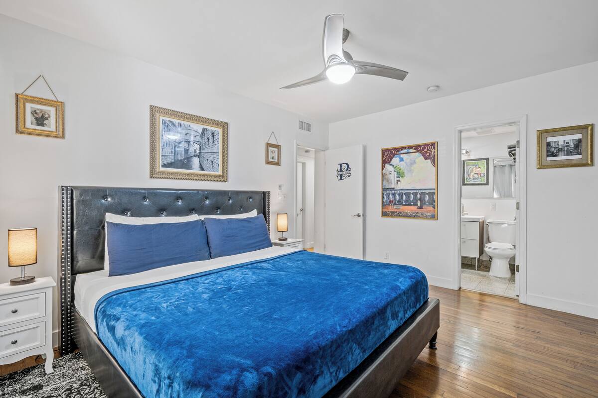 A bedroom with a large bed, a ceiling fan, and framed pictures on the walls.