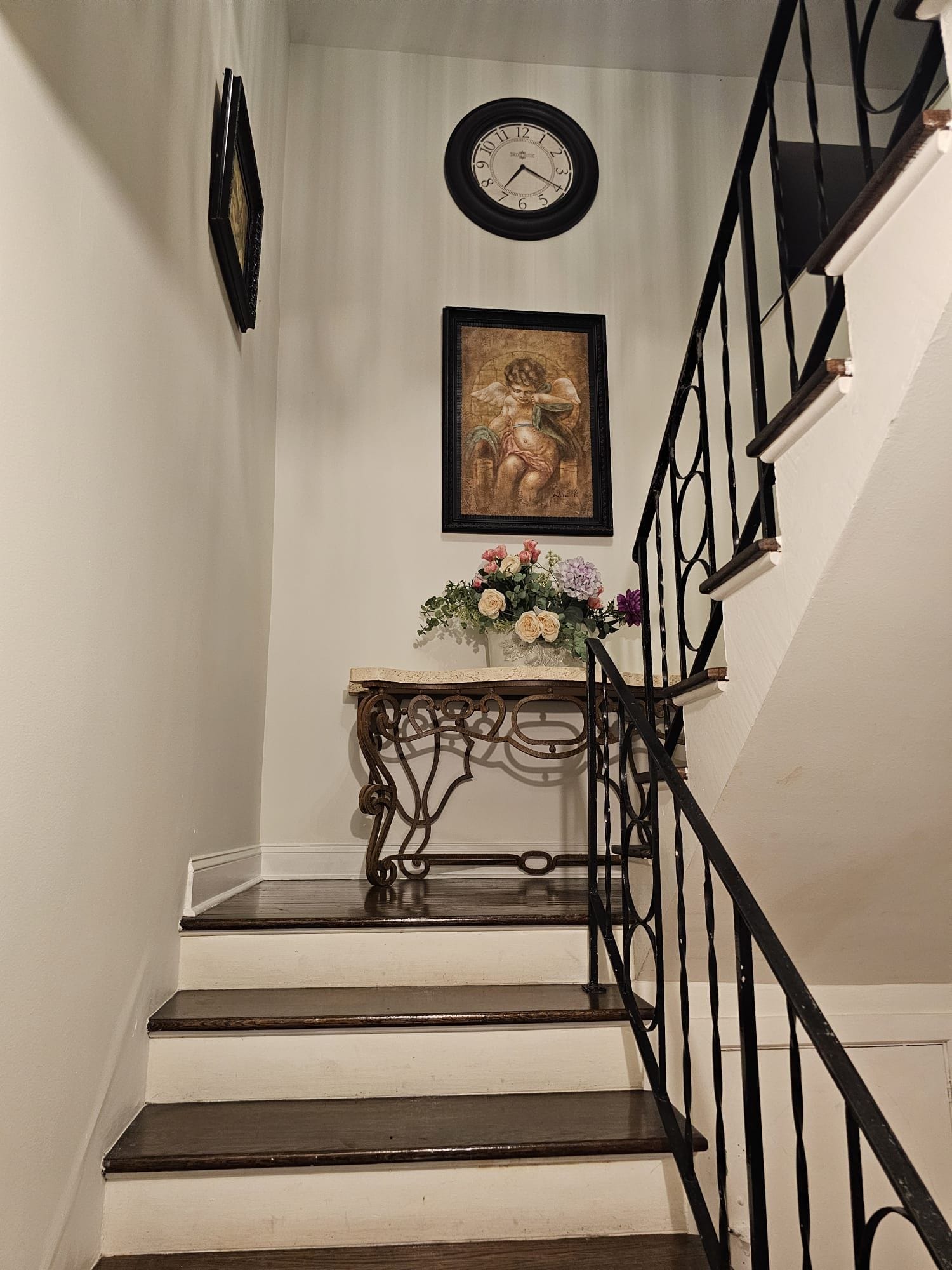 A staircase with a black railing, a clock, and a framed artwork above it.