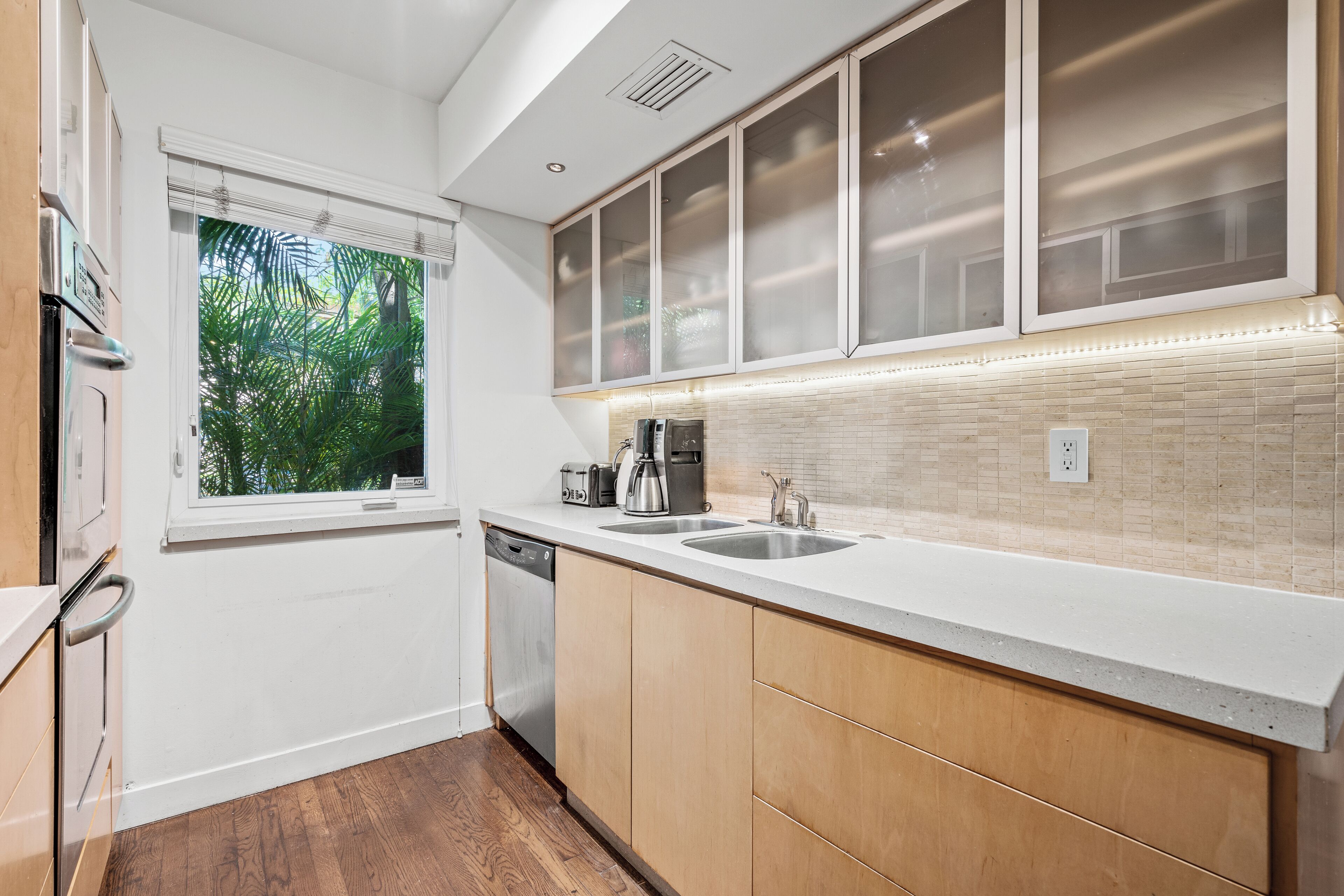 Una cocina moderna con lavavajillas, una ventana con vistas a la vegetación y una encimera con hervidor y tostadora.