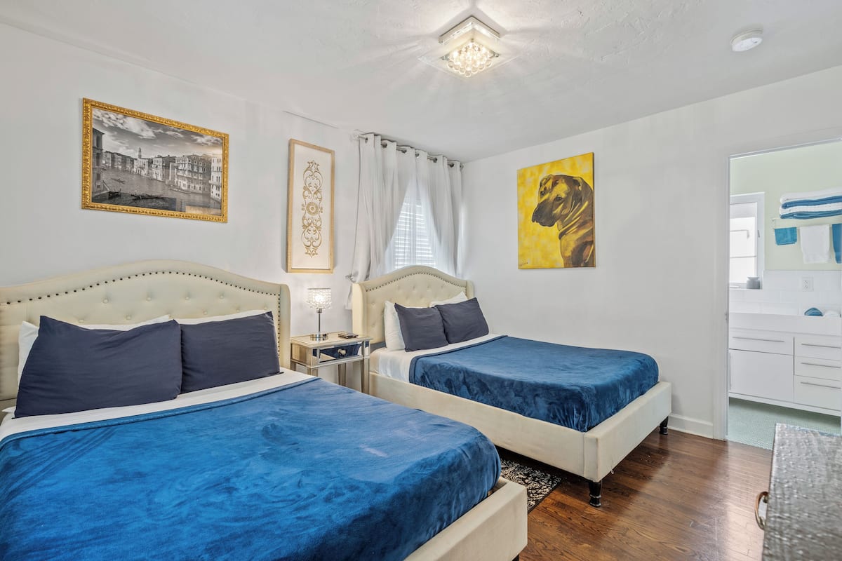 A hotel room with two beds, a nightstand, a lamp, and artwork on the walls.