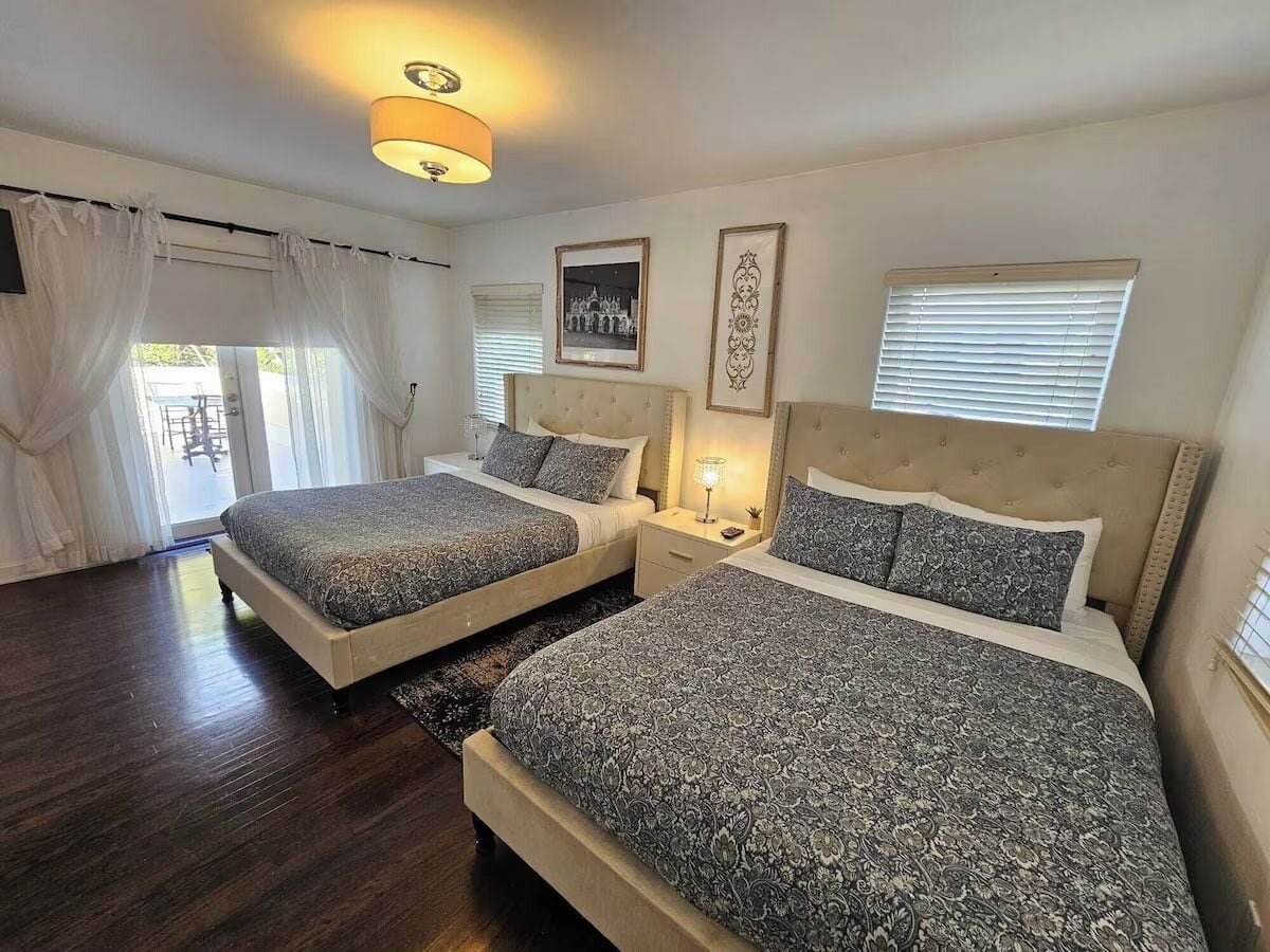 A bedroom with two beds, a chandelier, and a window with blinds.