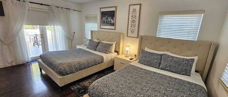 A bedroom with two beds, a chandelier, and a window with blinds.