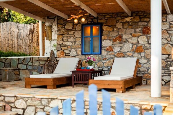 A stone-walled outdoor seating area with two wooden lounge chairs and a small table.
