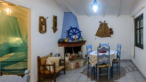 A room with a bed, a table with chairs, a fireplace, and a window. - Blue Seaside Retreat - Fully Equipped Garden Gem (Chrani)