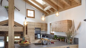 A modern kitchen with wooden beams, a large window, and hanging light fixtures. - Chalet Eggen (Zermatt)