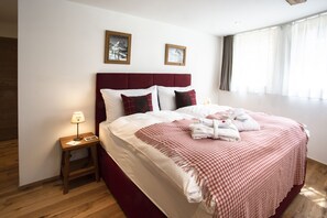 A neatly made bed with a checkered bedspread, a wooden nightstand with a lamp, and two framed pictures on the wall. - Chalet Eggen (Zermatt)