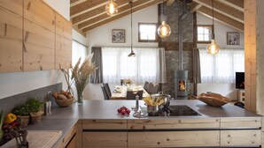 A modern kitchen with wooden beams, a central island, and hanging pendant lights. - Chalet Eggen (Zermatt)