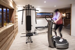 A gym with exercise equipment, a wooden wall, and a poster on the wall. - Chalet Eggen (Zermatt)