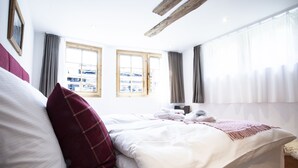 A hotel room with a bed, two windows, a wooden ceiling beam, and a view of the outside. - Chalet Eggen (Zermatt)