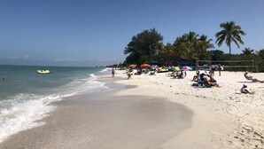 Ein Strand mit entspannten Menschen, Sonnenschirmen und einem klaren Himmel.