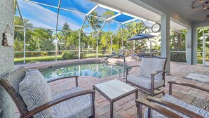 Ein Poolbereich mit Glasveranda, Sitzgelegenheiten im Freien und Blick auf Pool und Grünflächen.