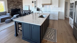 A modern kitchen with a large island, white cabinetry, and a stone fireplace. - Amazing Mountain, Lake and Island Views Private Beach,Fire Pit, Hot Tub, Kayaks  (Six Mile)