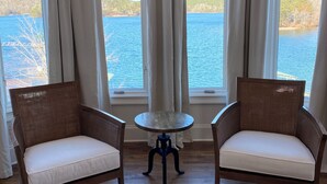 A room with two wicker chairs, a small round table, and a view of a lake through large windows. - Amazing Mountain, Lake and Island Views Private Beach,Fire Pit, Hot Tub, Kayaks  (Six Mile)