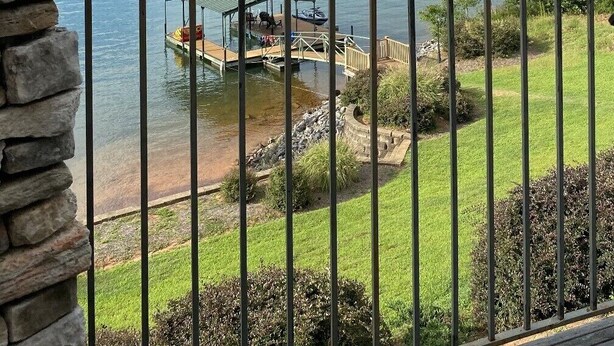 A lakeside view from a balcony with a dock, a small island, and distant mountains. - Amazing Mountain, Lake and Island Views Private Beach,Fire Pit, Hot Tub, Kayaks  (Six Mile)