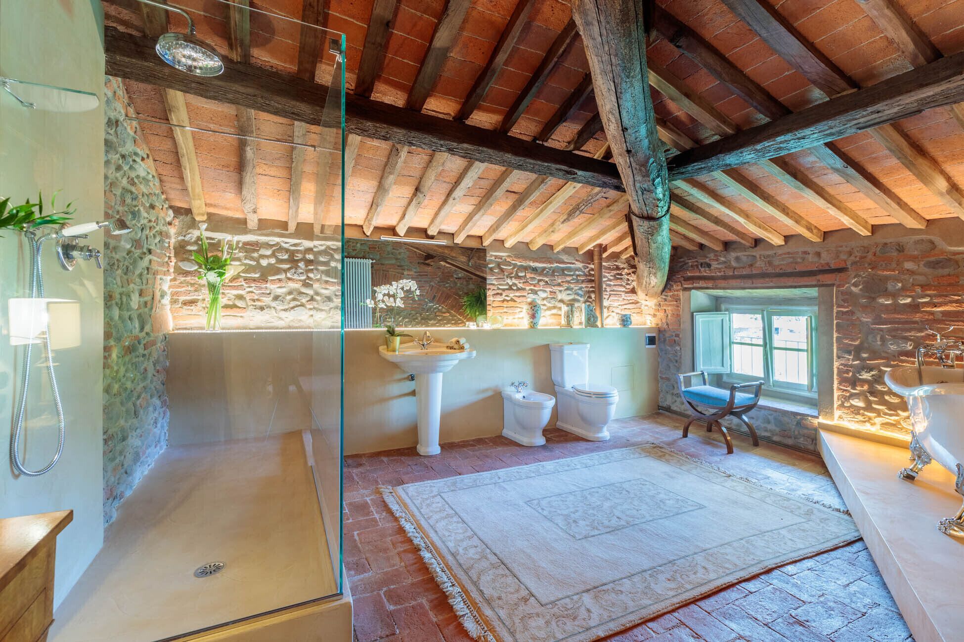 Une salle de bain rustique avec un mur en pierre, un plafond en bois et une grande fenêtre.
