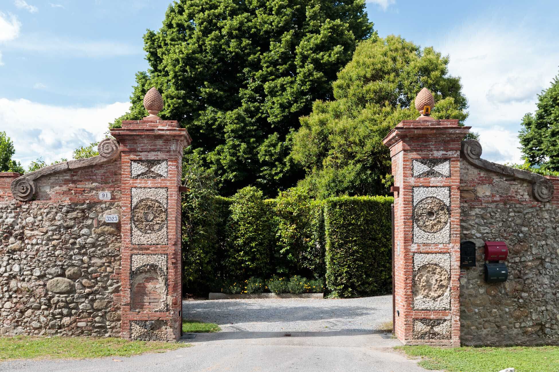 A stone gate with decorative brickwork and a large tree in the background.
