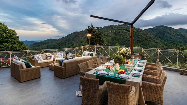 An outdoor dining area with wicker furniture and a table set for a meal, overlooking a mountainous landscape. - CASOLARE DEI COLLI Panoramic Private Pool, Lavish Interiors and a Gourmet Kitchen (Camaiore)
