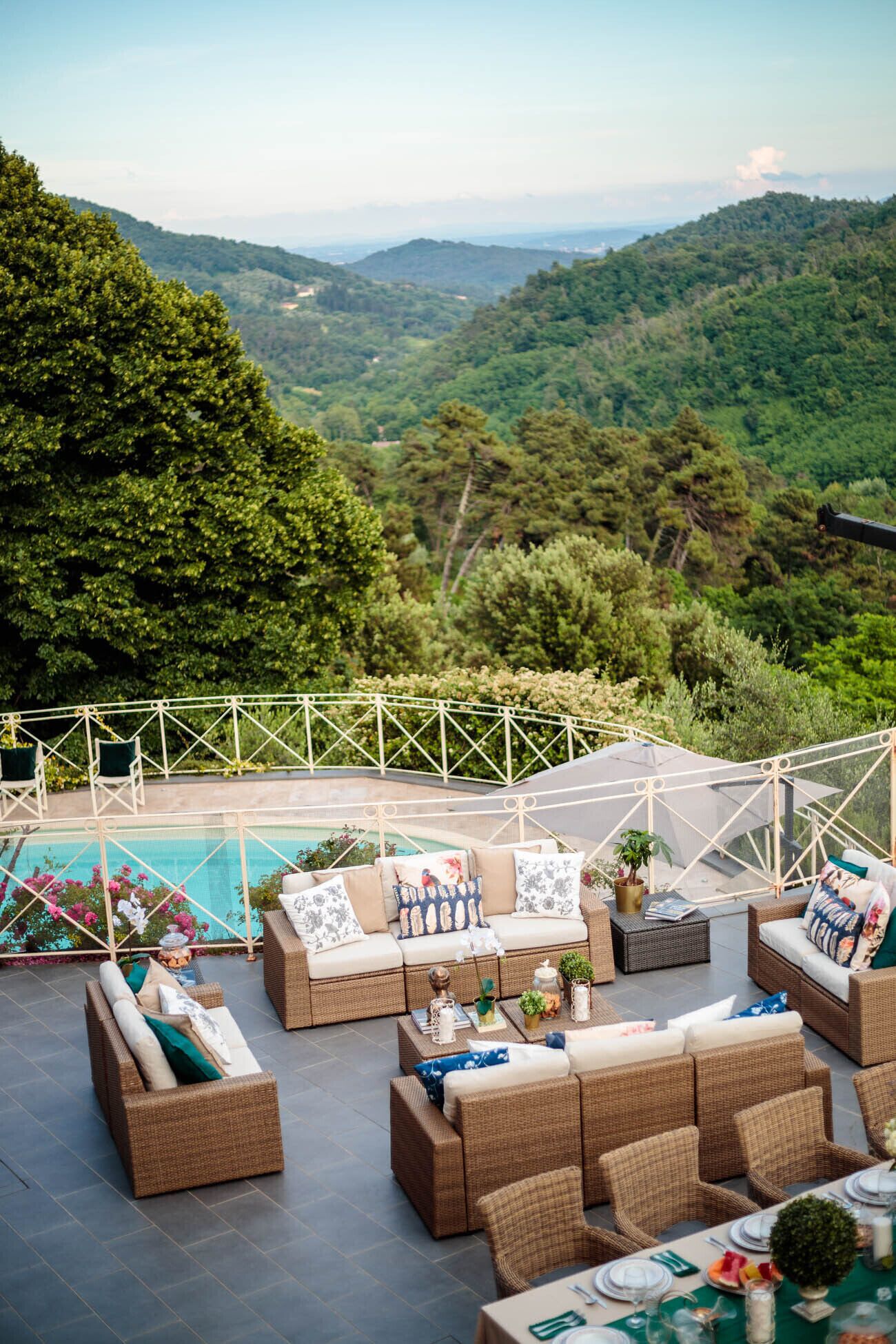 A terrace with wicker furniture, a pool, and a view of a mountainous landscape.