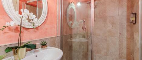 Ein Badezimmer mit einer begehbaren Glasdusche, einem weißen Waschbecken und einem großen Spiegel.