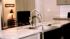 A kitchen with a double sink, a television in the background, and a 'HOME and HOME' sign on the wall.