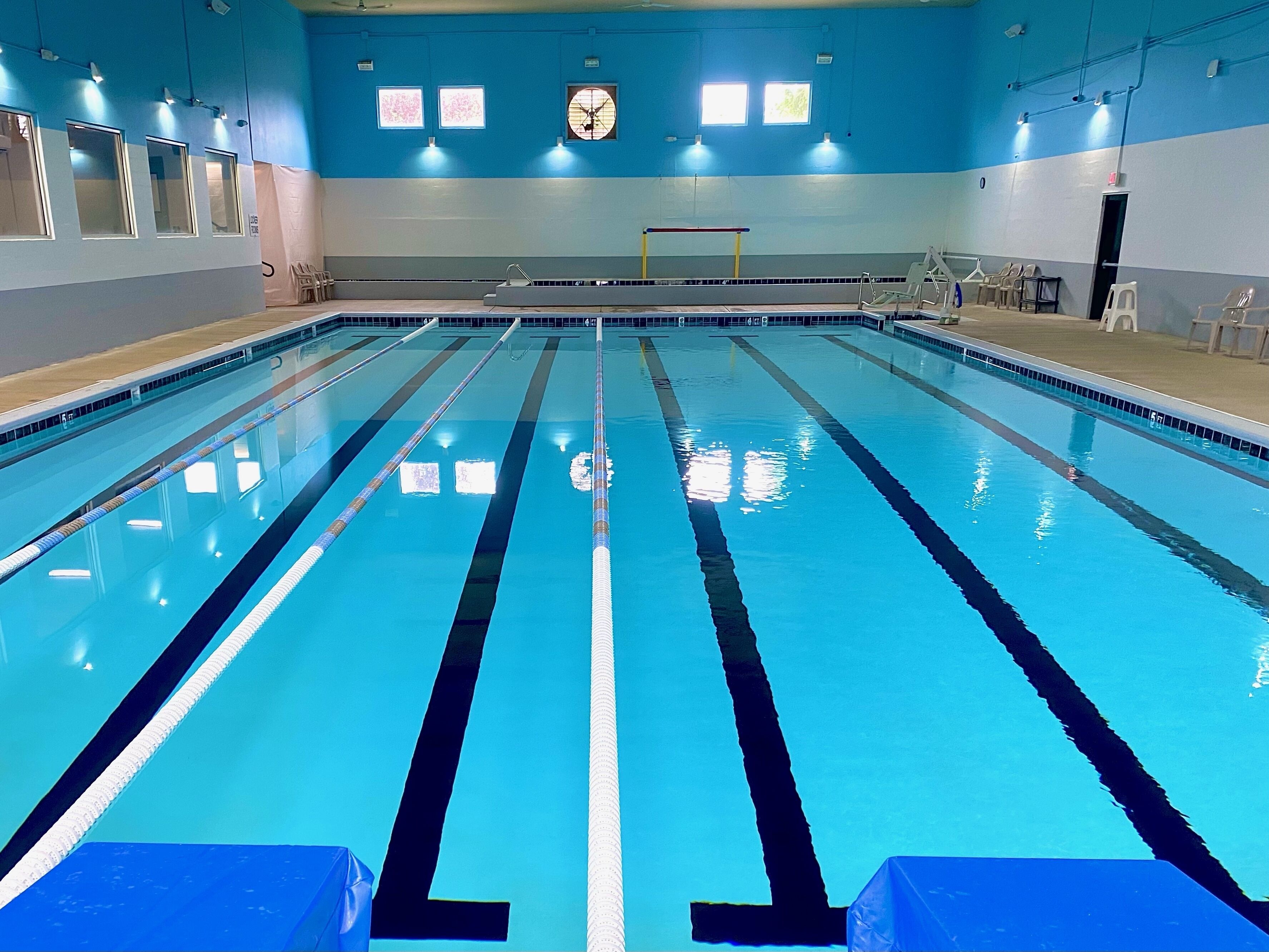 A large indoor swimming pool with clear lane markings, a diving board, and a set of stairs leading into the pool.