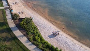 Una playa con un paseo marítimo pavimentado, una zona arenosa y algunas personas nadando.