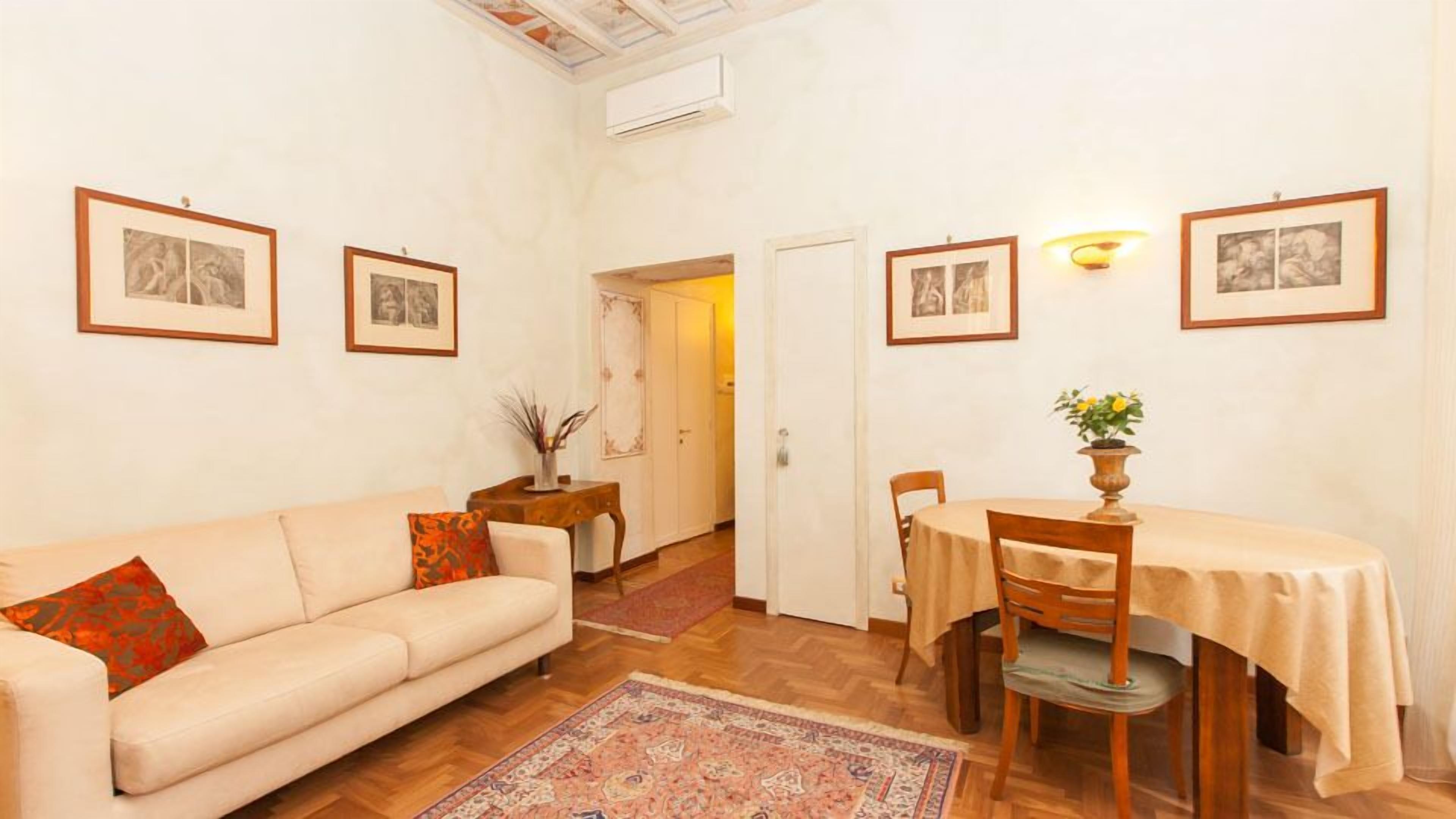 A living room with a sofa, a dining table with chairs, a rug, and framed pictures on the walls.
