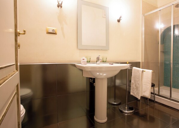 A bathroom with a white pedestal sink, a glass shower enclosure, and a towel rack.