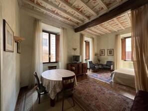 Um quarto espaçoso com uma mesa de jantar redonda, duas poltronas, um sofá e uma televisão.