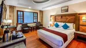 A hotel room with a large bed, two armchairs, a desk with a coffee maker, and a television. - Golden Metro Hotel (Bengaluru)