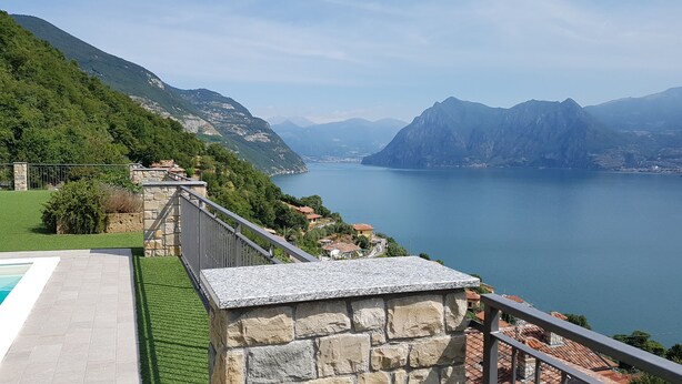 A stone balcony with a stone railing overlooking a lake with mountains in the background.