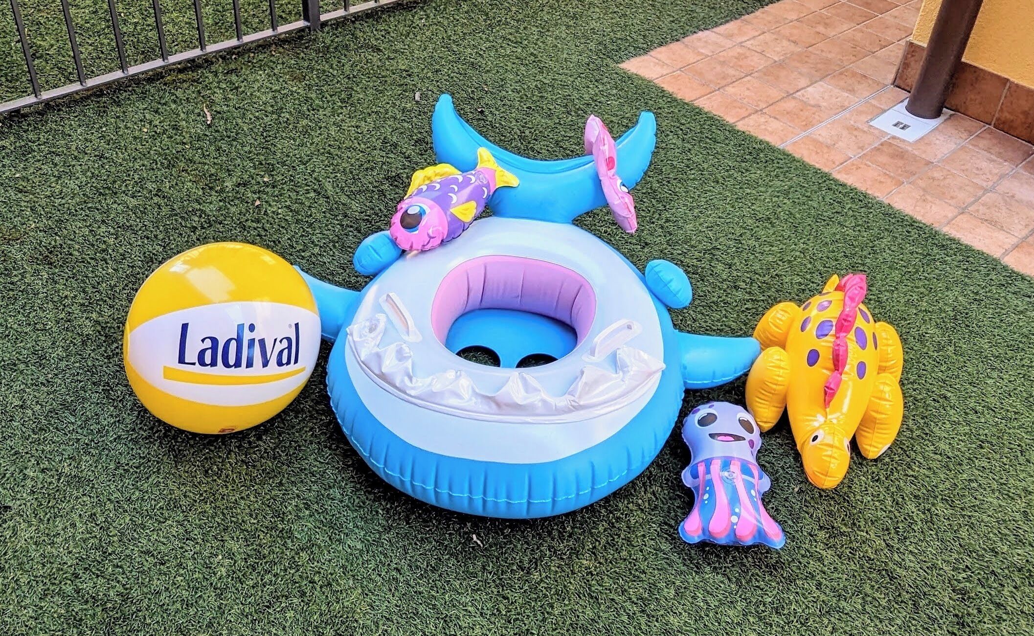 Una piscina gonfiabile con motivo blu e bianco, circondata da vari giochi colorati e un pallone giallo con la scritta 'Ladival'.