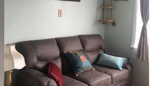 Ein Wohnzimmer mit einem braunen Sofa, einer Lampe und zwei Bildern an der Wand.