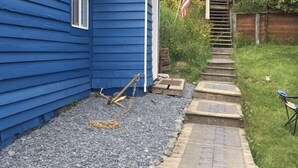 Ein blaues Haus mit einem kleinen Gartenhaus, einem Kiesweg und einer Holztreppe, die zu einer Terrasse führt.