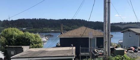 A small building with a flat roof and a porch, situated near a body of water with boats docked.