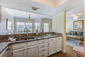A kitchen with a granite countertop, white cabinets, a double sink, and a ceiling fan.
