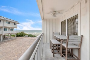 A balcony with a table and chairs, overlooking a beach.