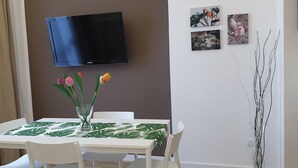 A dining area with a table set for four, a flat-screen TV mounted on the wall, and three framed artworks on the wall. - House with pool (Pompei)