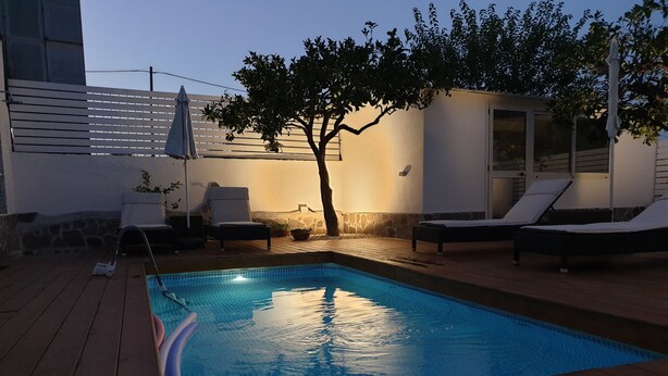 A swimming pool with lounge chairs and a tree, surrounded by a wooden deck and a stone wall. - House with pool (Pompei)