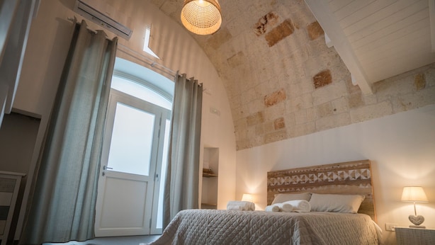 Un dormitorio con una cama grande, un cabecero de madera, una mesita de noche con lámpara y vistas al exterior a través de una ventana.