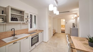 Una cocina moderna con armarios blancos, encimera de madera y horno empotrado. Hay una zona de comedor con una mesa y sillas de madera.