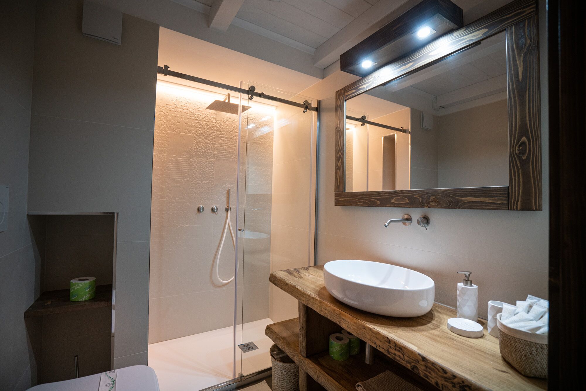 A modern bathroom with a glass-enclosed shower, a wooden vanity with a round sink, and a large mirror above the vanity.