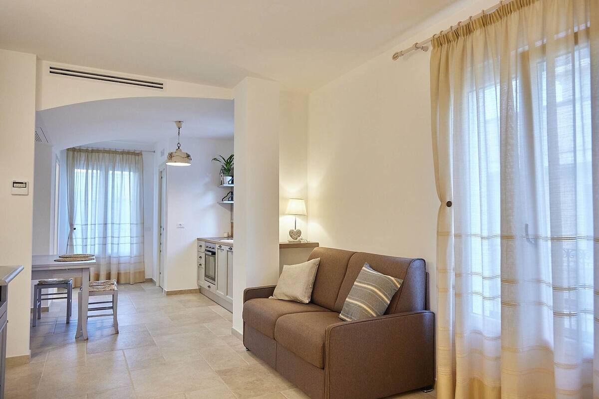 Ein Wohnzimmer mit einer Couch, einem Esstisch mit Stühlen und einer Küche im Hintergrund.
